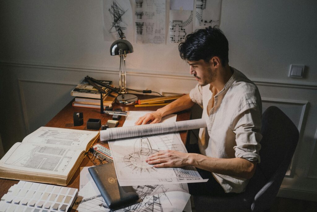 Young architect at a desk working on blueprint designs under lamp light.